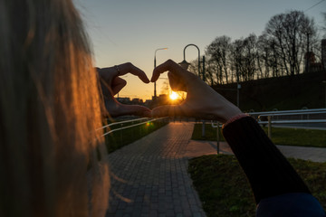Fototapeta na wymiar Blond woman holding hands as heart shape with beautiful sky in a warm color sunset