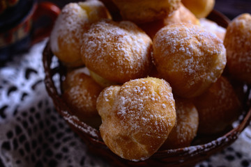 Fresh handmade profiteroles in a wicker basket on a lace doily in a ray of light, macro