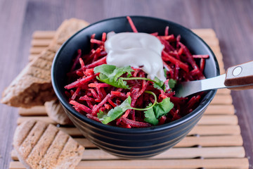 Thinly sliced ​​fresh beets in a black salad bowl with sprigs of cilantro ready for eating are on a wooden table, closeup.