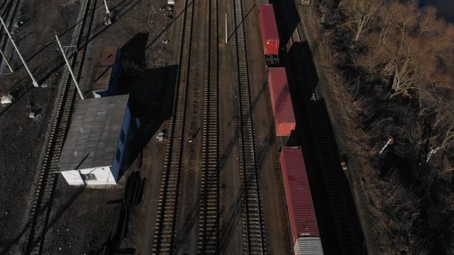 Aerial view of a large train on the rails next to the river. The camera flies over a long train of tanks standing on the rails