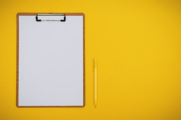 Paper on Clipboard and Pen on Yellow Background