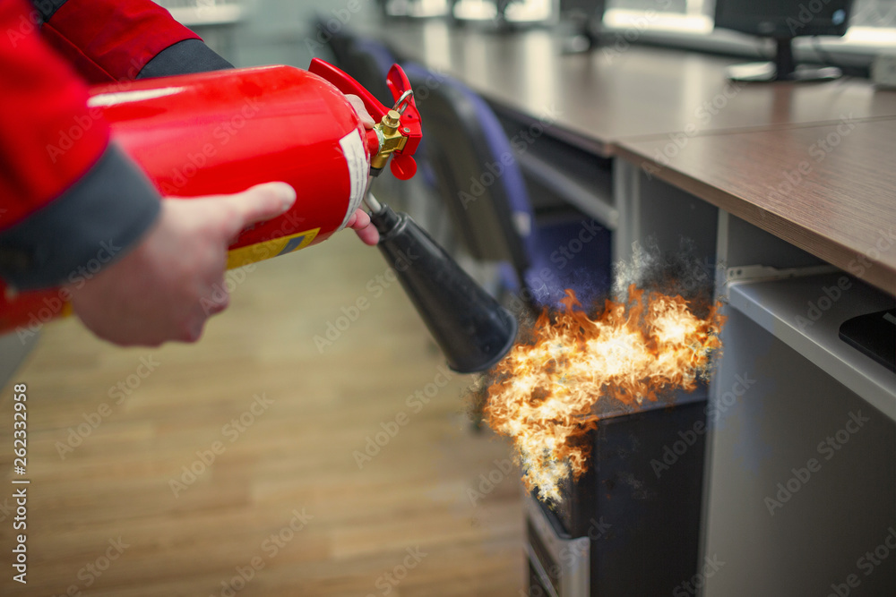 Wall mural a man practices how to use a powder type extinguisher in the office. the rescuer puts out the comput