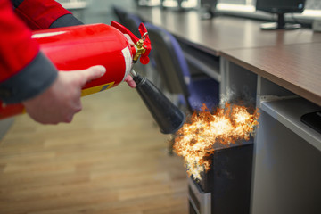 A man practices how to use a powder type extinguisher  in the office. The rescuer puts out the computer - obrazy, fototapety, plakaty