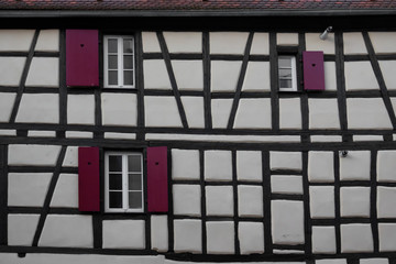 White wall of a traditional old half-timbered house. Alsace. France. There are black beams, windows and purple shutters. Background. Texture.