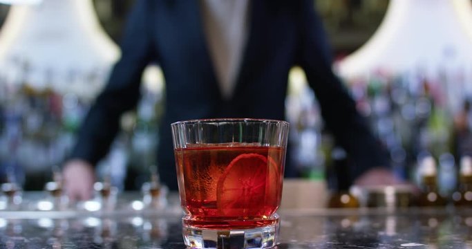 Bartender sliding oldfashioned negroni cocktail to a client. Close up shot on 6k RED camera.