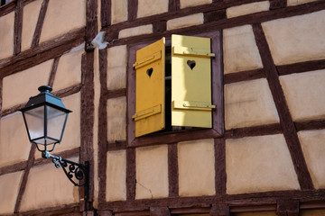 Fragment of the wall of a traditional half-timbered house. There is a window with yellow shutters and a street lamp. Background.