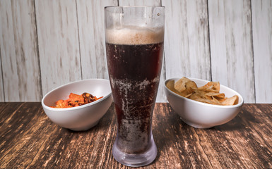 Two bowls of chips and a beer on a bar.