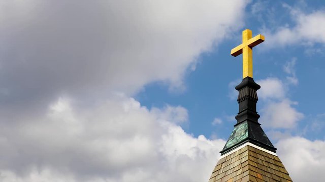 Cross on STeeple Cloud Time Lapse Loop - One minute looping video features a golden cross atop a church steeple with clouds moving at a moderate time lapse rater with a deep blue sky behind.