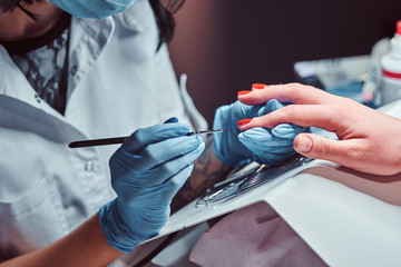 Beautician making long transparent artificial nails to a female client. Manicure procedure in a...