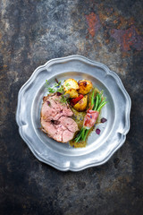 Barbecue marinated Greek lamb roast with potatoes and beans rolled in bacon as top view on a pewter...
