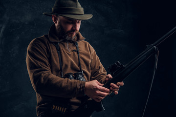 Opening of the spring hunting season. Hunter ready to hunt and charging a hunting rifle. Studio photo against a dark wall background