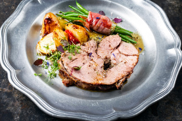 Barbecue marinated Greek lamb roast with potatoes and beans rolled in bacon as closeup on a pewter plate