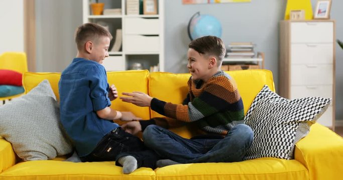 Caucasian two teen boys fighting on the yellow couch in the cozy room while playing.
