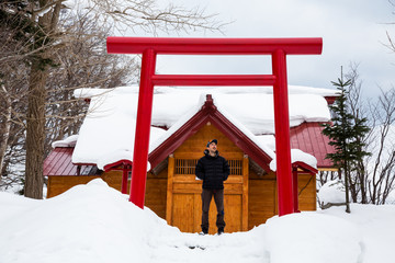 Man standing below red gate to Japanese building, ancient architecture style church or temple.