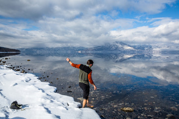 Man walking over snow into calm water of reflective lake. Lake Shikotsu of Hokkaido, Japan.