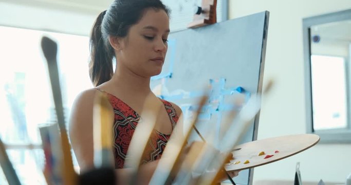 Portrait of hispanic woman painting, girl busy with artistic activity and exercising at home with paint, brush, easel, color. Young latino people and job, art profession, artist, hobby, lifestyle