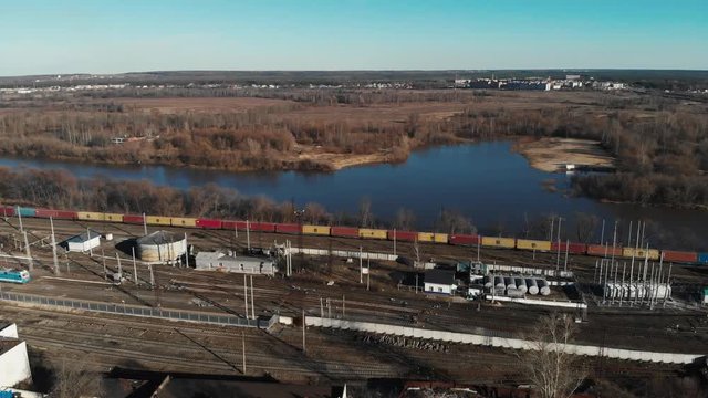 Aerial view of a large train on the rails next to the river. The camera flies up to a long freight train standing on the rails