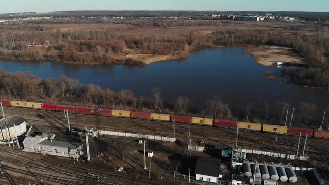 Aerial view of a large train on the rails next to the river. The camera flies up to a long freight train standing on the rails