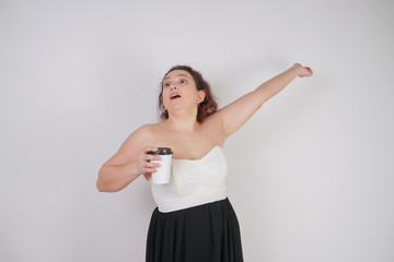 feminine woman with plus size body in a fashionable dress holding a paper Cup of coffee and posing on a white background in the Studio