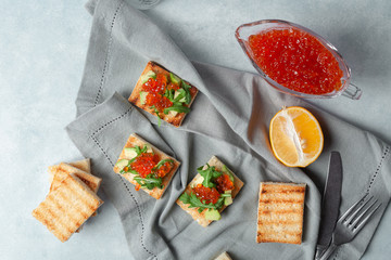 Toast with caviar, avocado arugula. On a gray concrete background