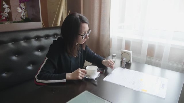 Young wonam use mobile phone while sitting in comfortable coffee shop during work break, charming happy female reading fashion news on cell telephone during breakfast in restaurant.