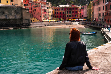 Fototapeta na wymiar Girl is sitting at the harobr of Vernazza and looking the awesome village of Vernazza, Cinque Terre, Liguria, Italy