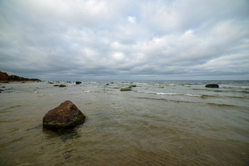Naklejka na ściany i meble stormy sea beach with large rocks in the wet sand