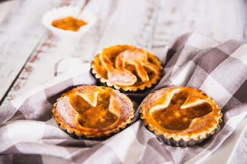 Tartlets sprinkled with powdered sugar with peach jam on white wooden background with kitchen towel