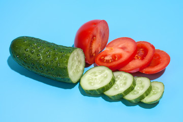 Ripe green cucumber and red tomato on blue background. Healthy eating and dieting concept.
