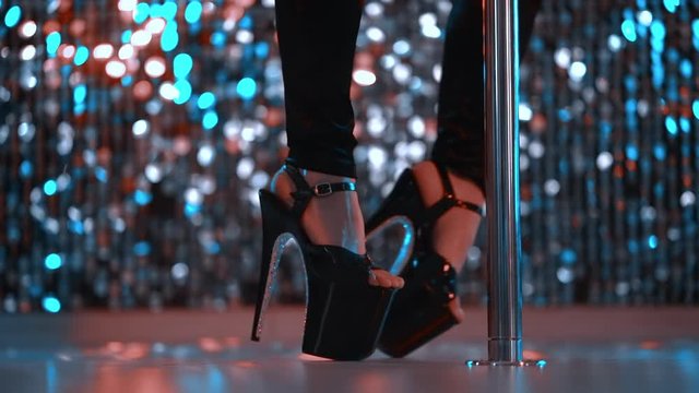 Young sexy striptease dancer moving in high heels shoes with rhinestones on stage with pylone in strip night club, Pole dancing. Shining background. Dance, sex, temptation concept