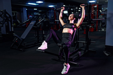 Fototapeta na wymiar Athletic sexy woman doing exercise using machine in gym - side view.