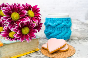 Maroon chrysanthemum. Pink flowers with a yellow center lie on the book. Nearby is a cup of tea, and delicious coffee. Pink gingerbread cookies are like dessert.