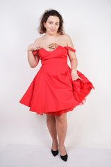 pretty chubby fashion girl wearing red pinup dress and posing with tasty colorful lollipop on white studio background