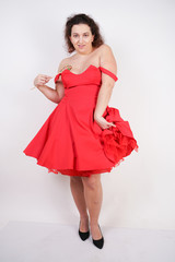 pretty chubby fashion girl wearing red pinup dress and posing with tasty colorful lollipop on white studio background