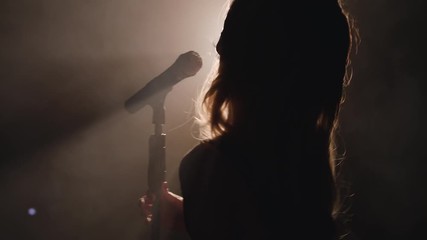 Close-up of the face of the singer with microphone on a black smoky background. The singer sings a song on stage in the dark, smoke, purple light, concert 4k - Powered by Adobe