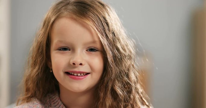 Close up of the cute and beautiful Caucasian little girl turning her head to the camera and smiling joyfully. Indoor. Portrait.