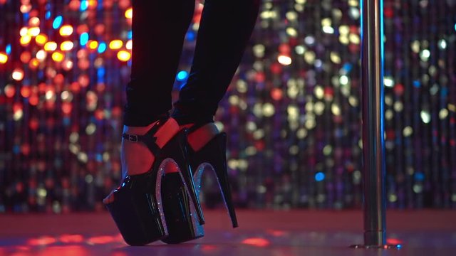 Young sexy striptease dancer moving in high heels shoes with rhinestones on stage with pylone in strip night club, Pole dancing. Shining background. Dance, sex, temptation concept