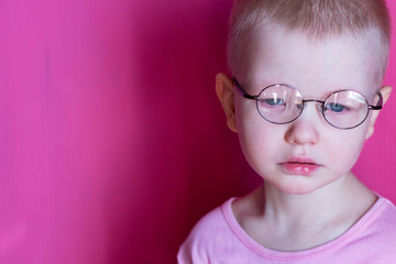 Fototapeta premium Happy blond child posing in room over pink background. Kid takes off and puts on glasses for fitting