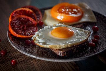 Grain bread with fried egg, tomato, cheese and bacon on ceramic plate with red orange 