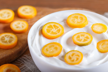 greek yogurt with kumquat pieces in a white plate on a brown wooden background