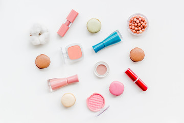 Make-up artist desk with powder, nail polish, decorative cosmetics and macaroon cookies on white background top view