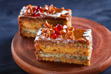 a piece of cake with caramel cream and poppy seeds on a wooden kitchen board, black background..