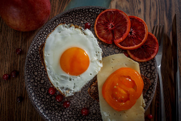 Grain bread with fried egg, tomato, cheese and bacon on ceramic plate with red orange 
