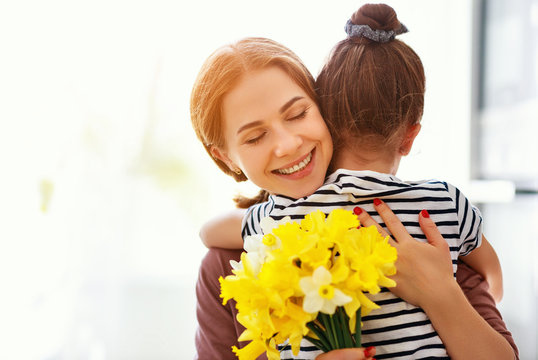 happy mother's day! child daughter   gives mother a bouquet of flowers to narcissus and gift.