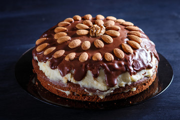 Homemade chocolate cake with milk cream and almonds on black wooden background.