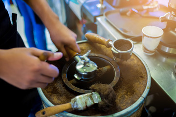 blurry hand pour ground coffee from machine into a wooden bucket with blurry coffee machine at bar counter in restaurant. Process of preparation of coffee, a closeup. Coffee machine espresso.