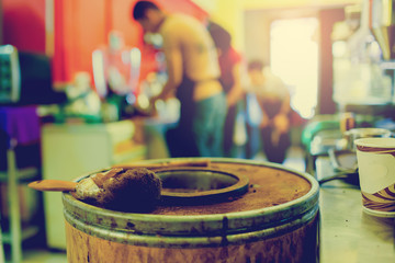 brush on wooden bucket of ground coffee from coffee machine with blurry staff at bar counter in restaurant or cafe background.