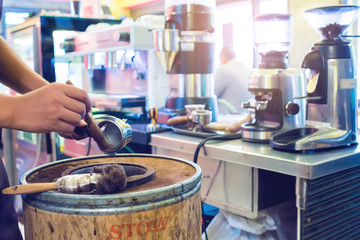 blurry hand pour ground coffee from machine into a wooden bucket with blurry coffee machine at bar counter in restaurant. Process of preparation of coffee, a closeup. Coffee machine espresso.