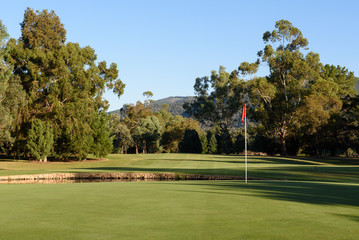 Golf flag on green looking back up fairway with gum trees and blue sky background at Bright golf course in Victoria Australia