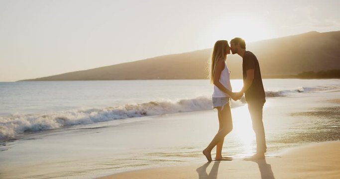 Young attractive couple kissing on the beach at sunset in slow motion, summer romance